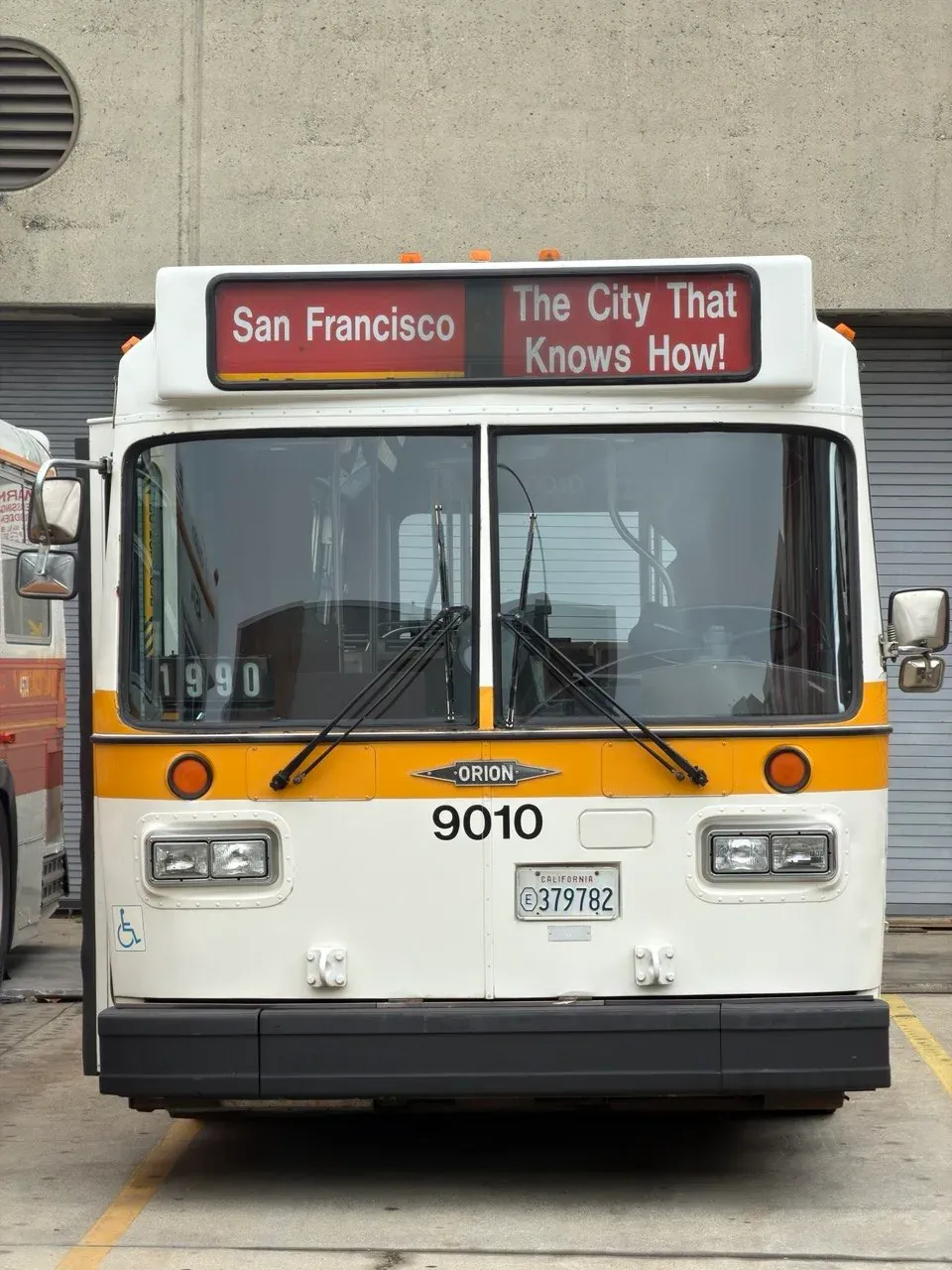 Front of a white bus with a yellow stripe, number 9010, its sign reading San Francisco, The City That Knows How!